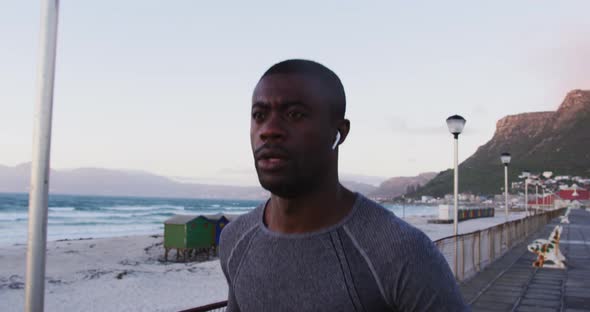 Focused african american man exercising outdoors, running by seaside with wireless earphones on