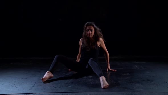 Young Female Modern Dancer Is Performing Dance Passionately, Sitting on Floor in Dark Studio