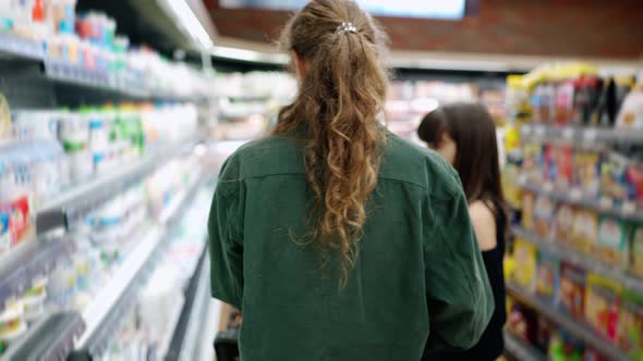 Teen Girl and Her Mom or Sister Shopping in the Supermarket with Cart Rear View