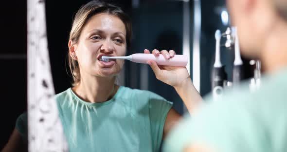 Young Woman Brushing Her Teeth with Electric Toothbrush in Front of Bathroom Mirror  Movie