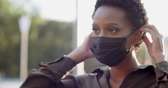 Portrait of Isolated Ethnic Girl Standing in Street Putting on Black Medical Mask on Female African