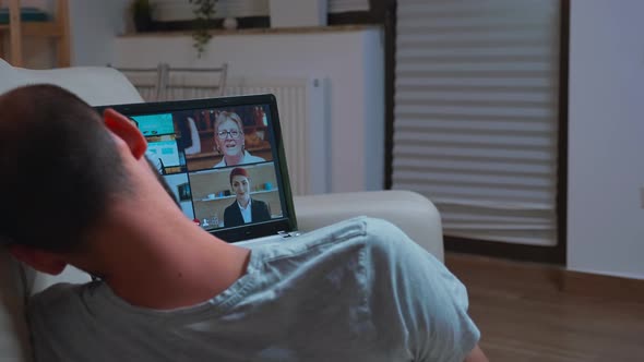 Tired Man in Pajamas Lying on Sofa While Falling Asleep During Videocall Conference