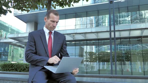 Middle Aged Businessman Working on Laptop Outside Office