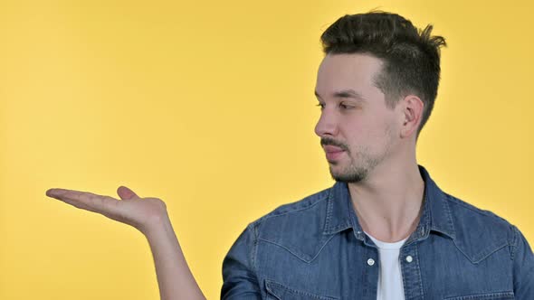 Portrait of Young Man Holding Product on Hand, Yellow Background