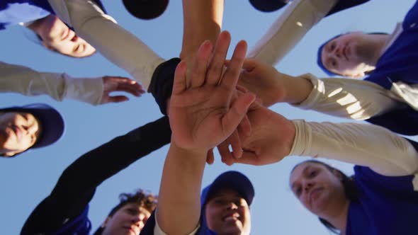 Low angle view of diverse group of female baseball players making hand stack against blue sky