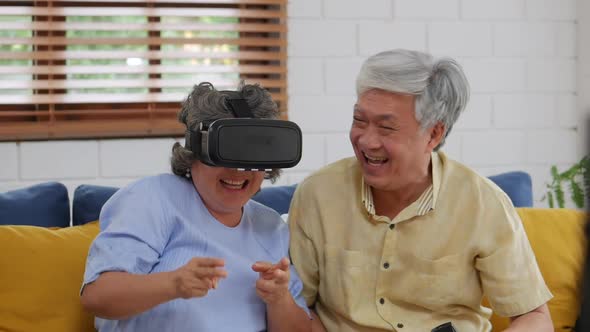 Smiling Asian senior couple playing games having fun at home using virtual reality.