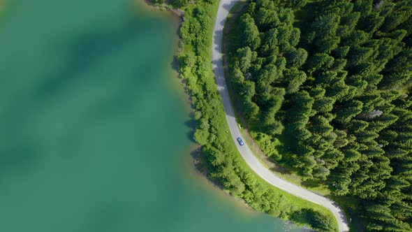 Aerial view of car driving through the fores and the lake on the side. Beautiful mountain road. 