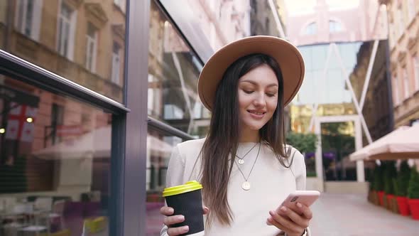 Joyful Young Woman in Stylish Hat Which Walking Between Modern Buildings with Street Cafe