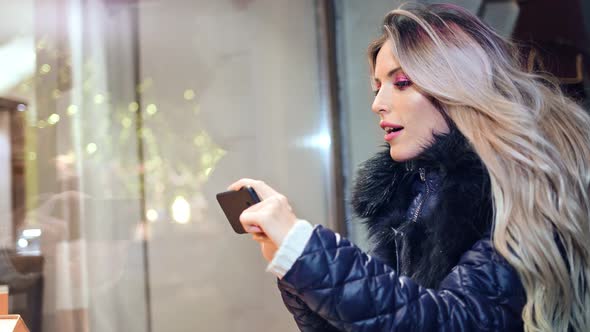 Enthusiastic Pretty Woman Taking Picture of Christmas Gift in Shop Glass Window Using Smartphone