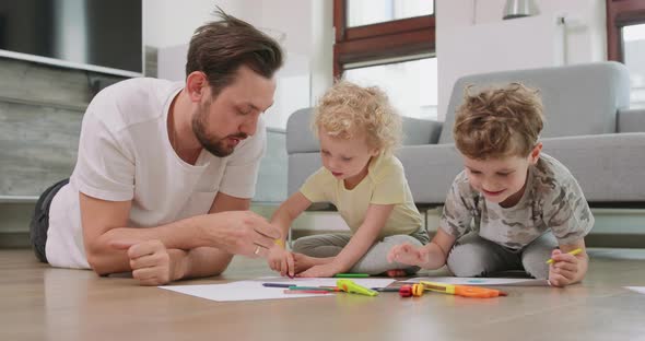 A Little Boy and a Little Girl and Their Father are Drawing with Pencils on the White Paper on the