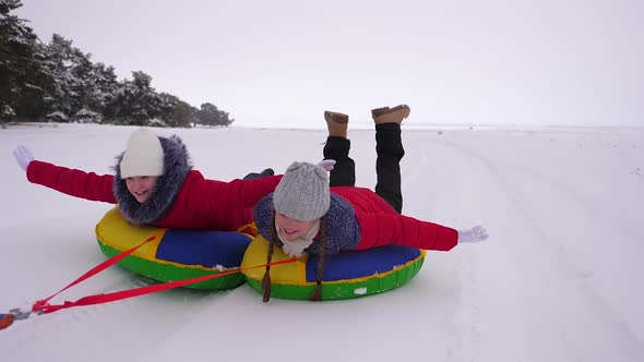 Children in Red Jackets Ride Through Snow in Winter on an Inflatable Snow Pipe