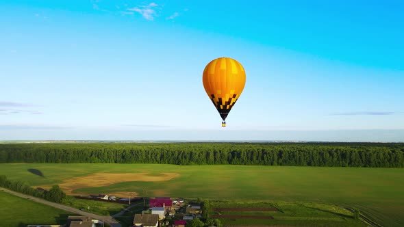 Air balloon with people in gondola flies over the field and casts a long shadow