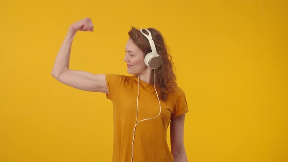 Happy Woman in Headphones Smiles and Shows Biceps on Hands