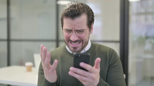 Portrait of Young Businessman Reacting to Loss on Smartphone