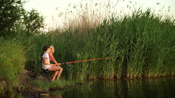 Little Girls Sitting with Fishing Rod on River Bank