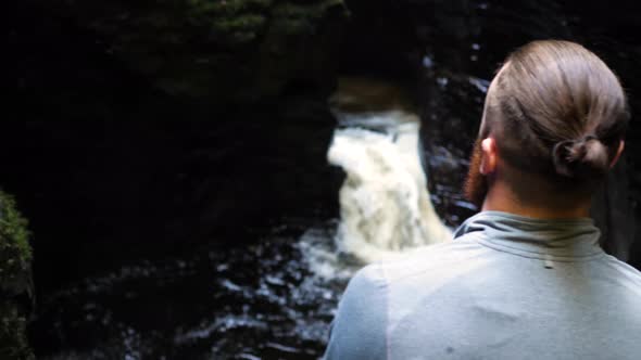 Back view of young man looking down on churning waters of a river