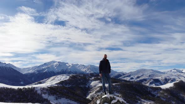 Aerial View of a Bearded Adult Male Tourist Standing on Top of a Snowcovered Cliff Looks Around