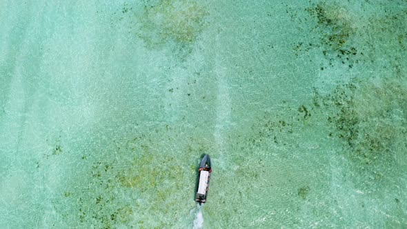 Motor boat sailing in shallow turqouise ocean waters, overhead shot.