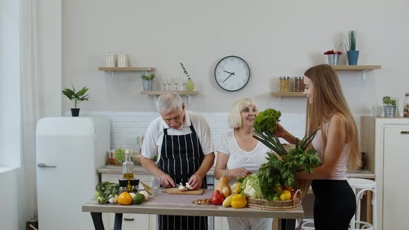 Senior Couple in Kitchen Receiving Vegetables From Granddaughter. Healthy Raw Food Nutrition