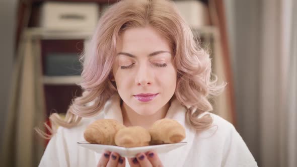 Portrait of Beautiful Caucasian Girl Smelling Tasty Croissants and Showing Plate To the Camera