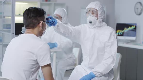 Doctor in Protective Suit Checking Temperature of Contagious Patient