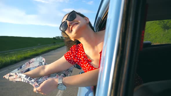 Young Girl in Sunglasses with Scarf in Her Hands Leaning Out of Window Retro Car and Rejoicing