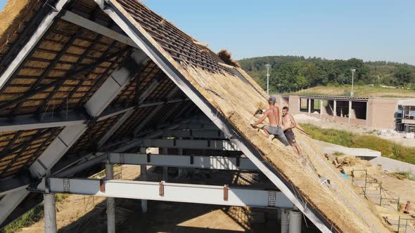 Aerial View the Roof of a Large House with Dry Straw and Hay. Workers Who Install the Roof.