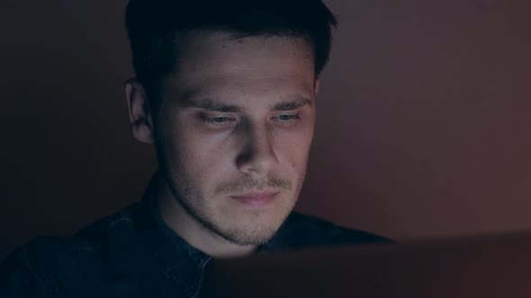 Portrait of a male working at the computer at night. Man browsing the Internet