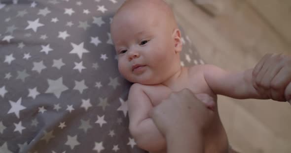 View of Little Baby Boy During Workout with Mom's Hands on a Big Fitball in Room