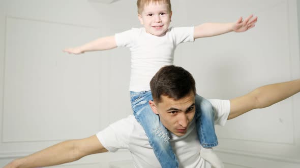 Dad Plays with Son Sitted on His Shoulders Depicting a Plane