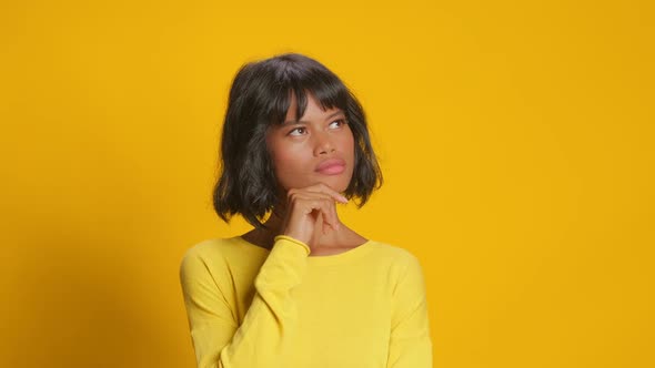 Young Woman Looks Somewhere Pensively Thinks Deeply Against Yellow Background