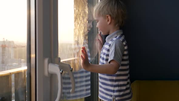 Small Blond Baby Kid Looking At Window Street Against Shine Sunset Rays