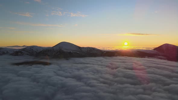 Aerial view of vibrant sunrise over white dense fog with distant dark peaks of Carpathian