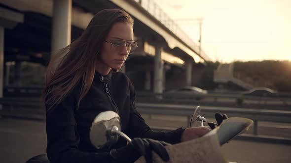 Caucasian Female Biker Examining Map Looking Far Away on Highway Sitting on Motorbike Under