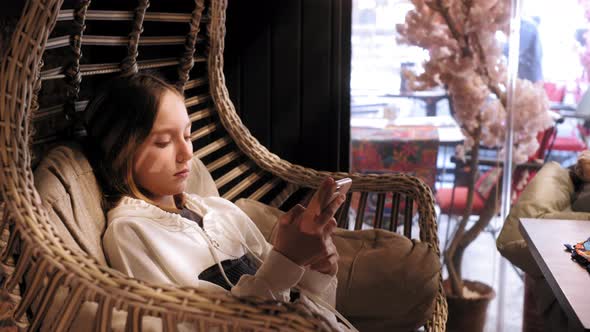 Young Girl Swaying in Cocoon Chair and Using Smartphone