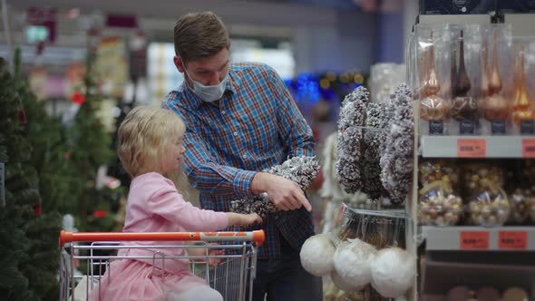 The Girl Sits in the Shopping Basket Chooses a Wreath with Her Father