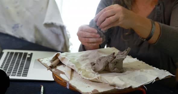 Mature female potter molding a clay while using laptop