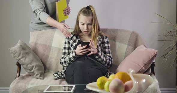 Portrait of Dissatisfied Teenager Using Smartphone As Her Unrecognizable Mother or Grandmother