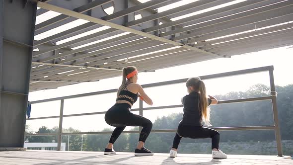 Young Woman and Little Girl which Doing Together Squat Exercises Near Handrail