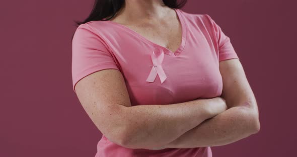 Woman with arms crossed wearing pink breast cancer awareness ribbon on t-shirt