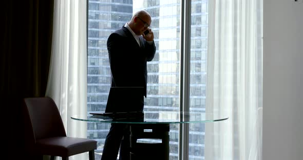 Silhouette of a Business Man in a Suit in Front of a Large Panoramic Window of the Business Center