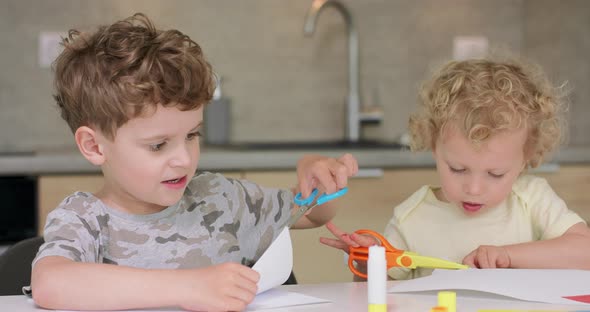 Brother and Sister are Cutting Different Objects From Paper with Scissors While Sitting at the Table