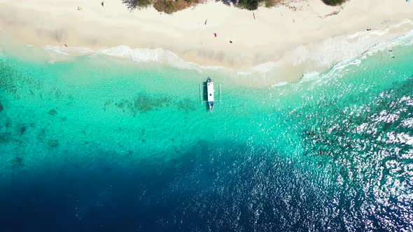 Top view of traditional boat anchoring on shoreline of tropical island with white sandy beach washed