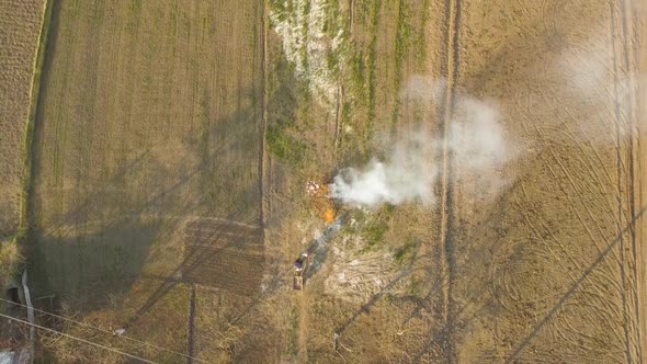 Drone View of People Leaving Burning Fire on the Field. Farmers Burning Dry Fallen Leaves and