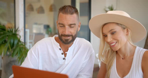 Loving Couple Sitting Outside at a Table and Having Live Stream with Their Friends Using Computer