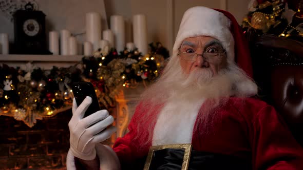 Shocked Santa Claus Looks at Smartphone Turns Head in Surprise Looks Camera