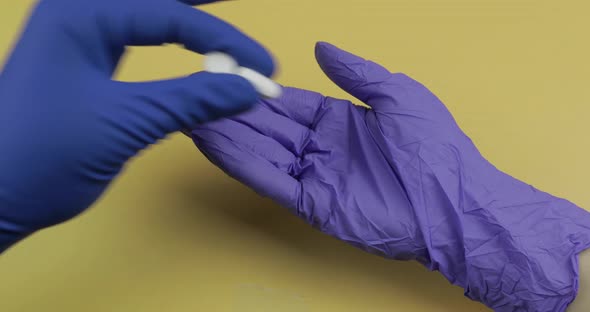 Hand Dressed in Blue Medical Glove Puts Two White Pill Into Other Hand