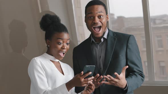 Young Excited Amazed African Colleagues Looking at Smartphone Screen Feel Overjoyed Euphoric with