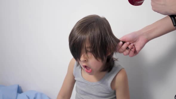 Mom Dries Long Wet Hair for Her Five Year Old Son in a Blue Bathrobe on a White Bed