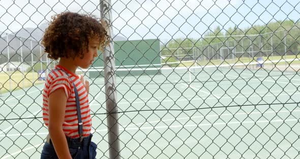 Side view of mixed-race schoolgirl walking near wire mesh fence at school 4k